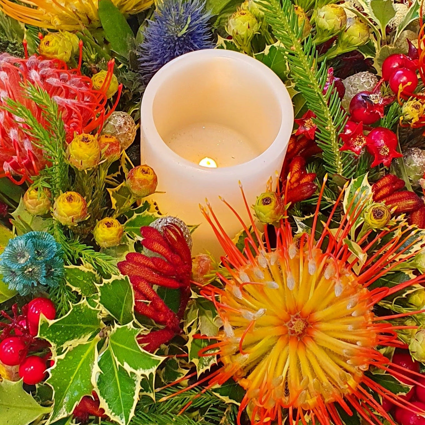 Decorative floral arrangement with a candle in the center on a reflective surface.