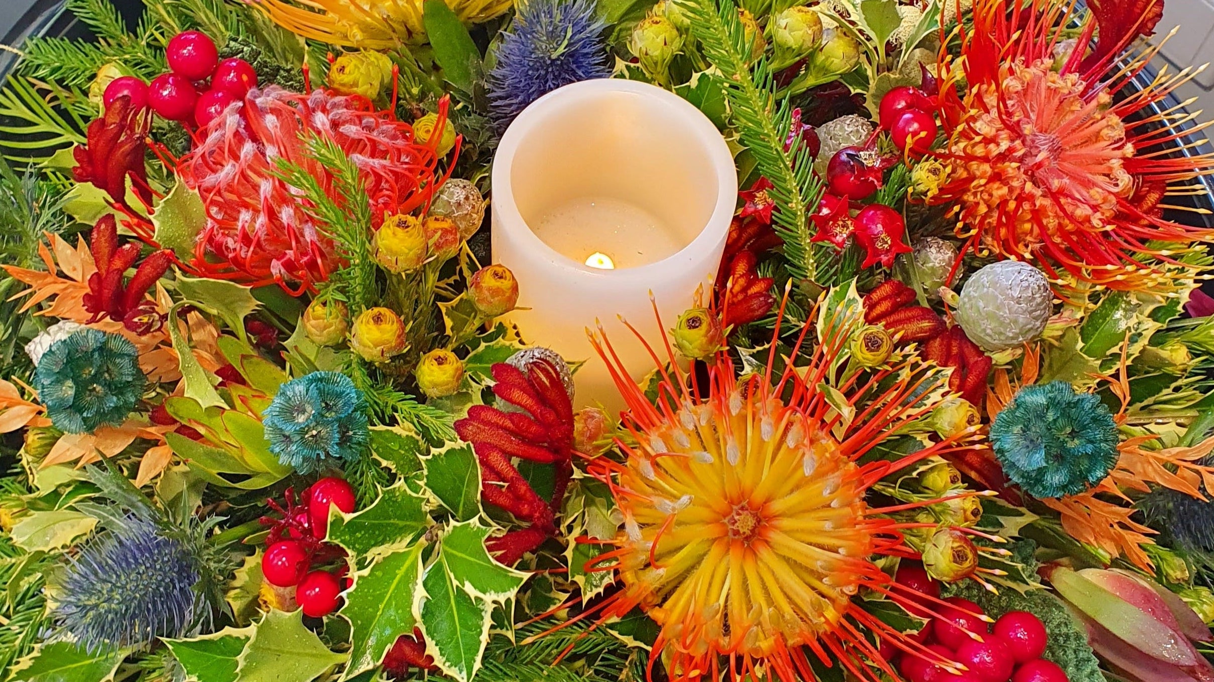 Decorative floral arrangement with a candle in the center on a reflective surface.